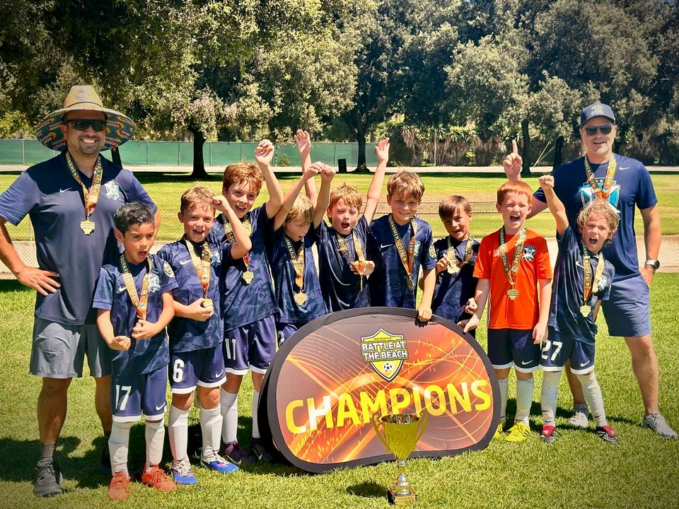 AYSO Region 84 Extra Play boys team and coaches cheering with medals behind their champions banner